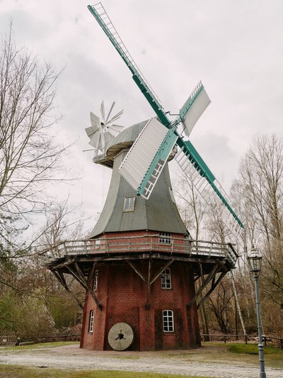 Die Holländermühle steht auf einem zweigeschossigen Steinsockel. Im Steinsockel sind mehrere Kastenfenster zu sehen. Auch der Körper der Mühle hat ein Kastenfenster. Die Mühlenflügel sind vorne an der drehbaren Kappe angebracht. Hinten sitzt ein Windrad.