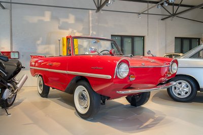 Das feuerrote Amphicar hat deutlich mehr Bodenfreiheit als ein normales Auto. Es sieht aus wie ein Cabrio und ähnelt im Design anderen Wagen der frühen 1960er Jahre: runde Glubschaugen-Scheinwerfer, angedeutete Flossen am Heck.