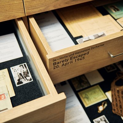 Blick in zwei geöffnete Schubladen mit Unterlagen, Briefen und Fotos. Auf einer Schublade ist zu lesen: Hella und Hannelore Zacharias. Barely Escaped, 20. April 1945