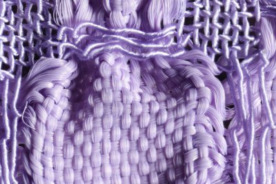 Detailaufnahme eines lilafarbenen Gewebes. Durch zwei unterschiedlich elastische Garne, Gummilitze und Seide, tritt das Blasenmuster des Stoffes besonders hervor. 
