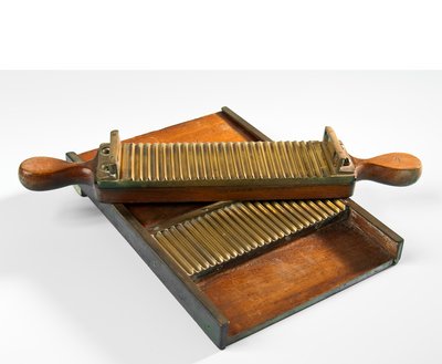 Das Pillenbrett aus Holz hat eine geriffelte Fläche. Darauf liegt ein ebenfalls geriffeltes hölzernes Handteil. Mit dem Handteil wurde die teigartige Arzneimasse vorsichtig über die Riffelung gerollt. So entstanden gleichmäßige Einzelportionen.