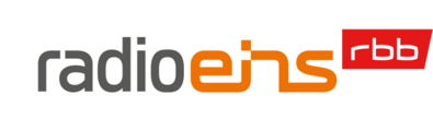Das Logo des Senders radio eins. Der Schriftzug "radio" in Grau, "eins" in Orange und daneben hochgestellt "rbb" in Weiß auf rotem Grund.