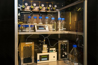 Der Oligosaccharid-Synthesizer ist in einen Laborschrank eingebaut. Auf zwei Ebenen stehen Messgeräte und Flaschen, die über Schläuche mit einem Ventilsystem verbunden sind.