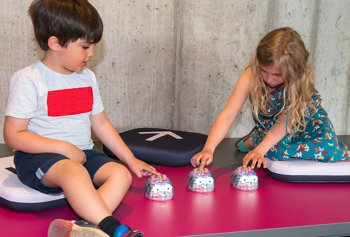Zwei Kinder lernen in den farbenfrohen Räumen des kids.digilab mithilfe von Robotikspielzeug zu denken und zu spielen wie ein Computer.