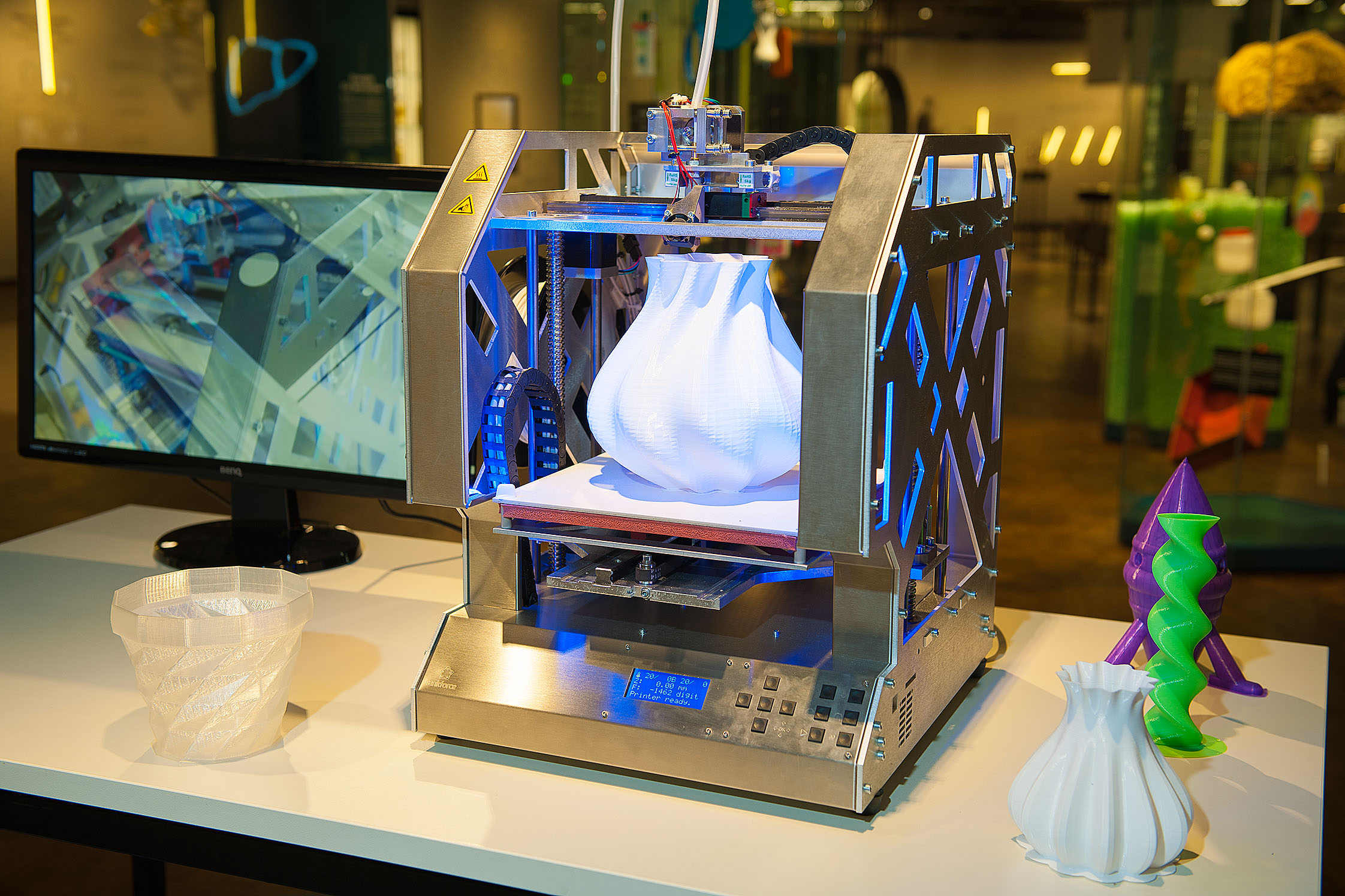 Ein 3D-Drucker aus silberglänzendem Metall. Darauf befindet sich eine weiße, gedruckte Vase.