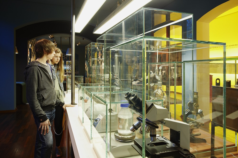 Ein Junge und ein Mädchen stehen neben einer Vitrine mit Mikroskopen und anderen Geräten.