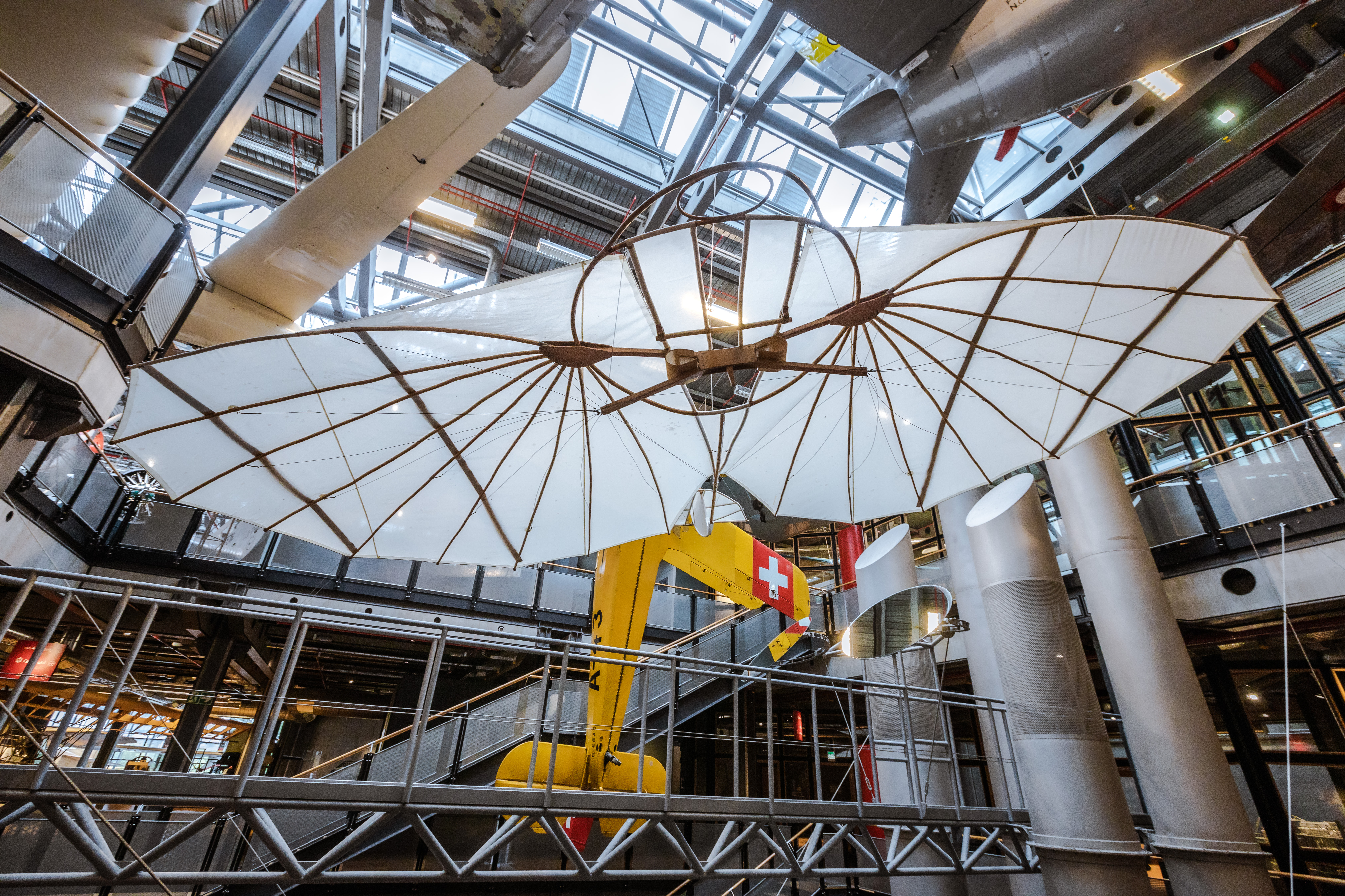 Im offenen Treppenhaus des Neubaus schwebt ein Segelapparat mit Holzgestell und aufgespannten, weißen Tragflächen.