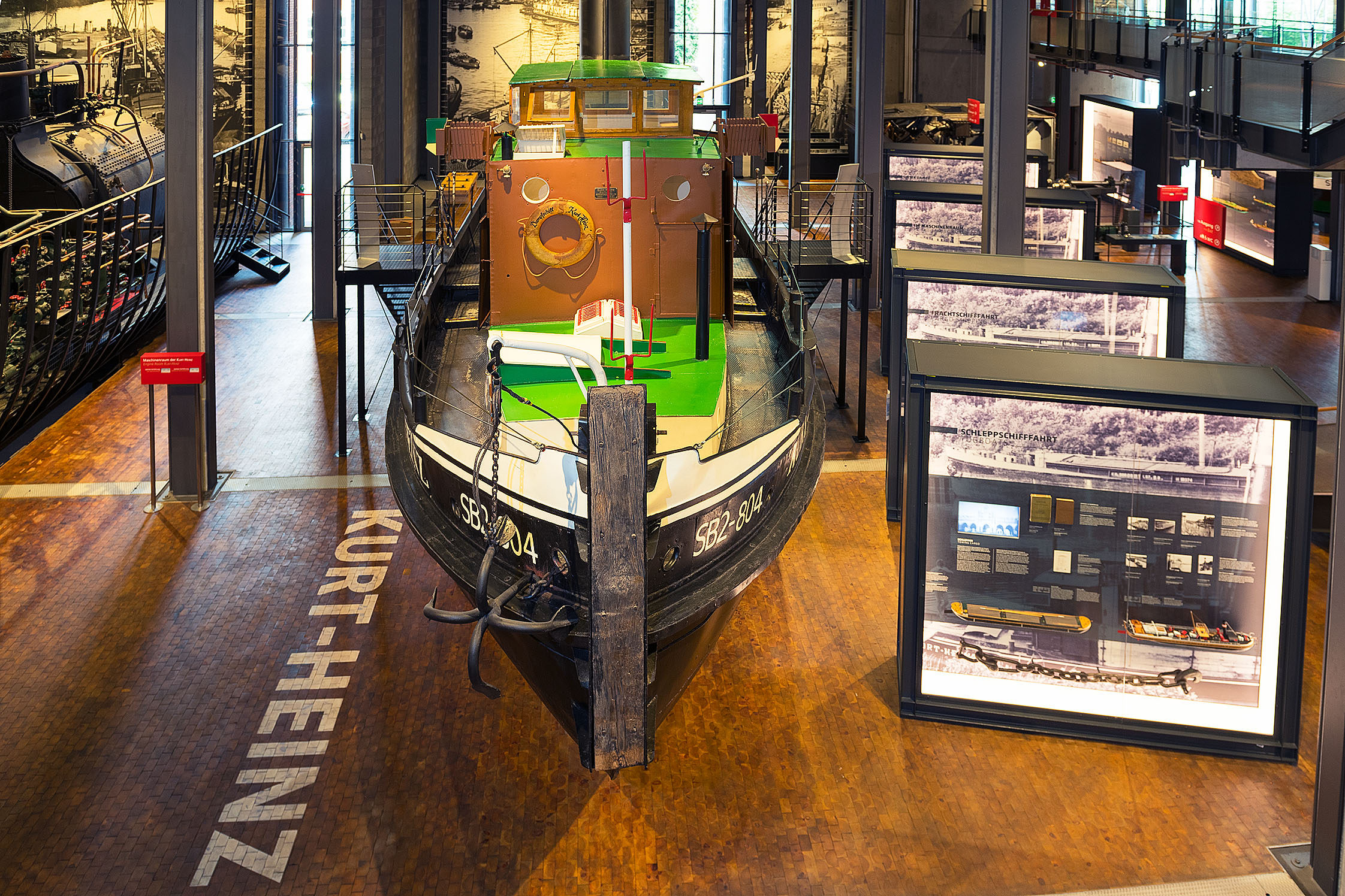 Ein kleines, historisches Dampfschiff steht in der Schifffahrt-Ausstellung. Daneben große Leuchtvitrinen. Seitlich ist der Schriftzug „SB2 -804“ und „Kurt-Heinz“ zu lesen. 