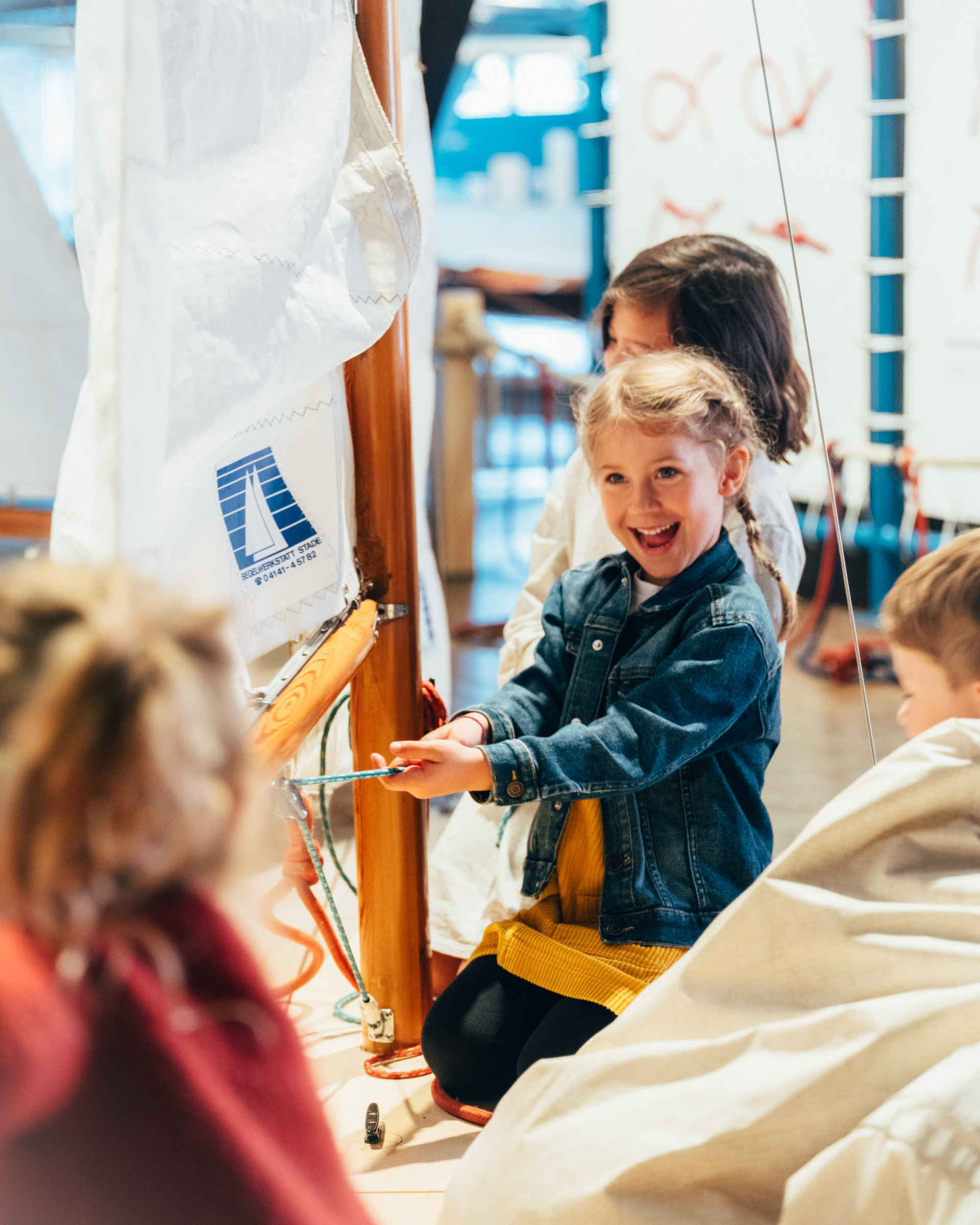 Drei kleine Mädchen hissen an einer Mitmach-Station die Segel eines Bootes.