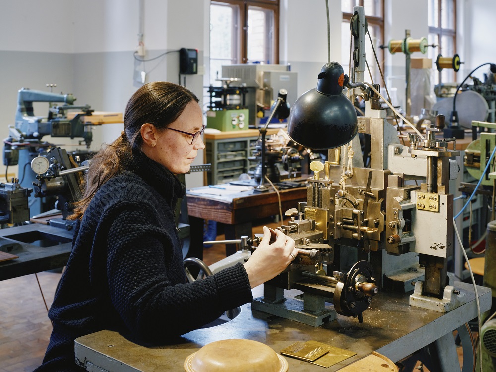 Eine Frau arbeitet an einer Maschine, die geometrische Formen in Metallstücke ritzt.