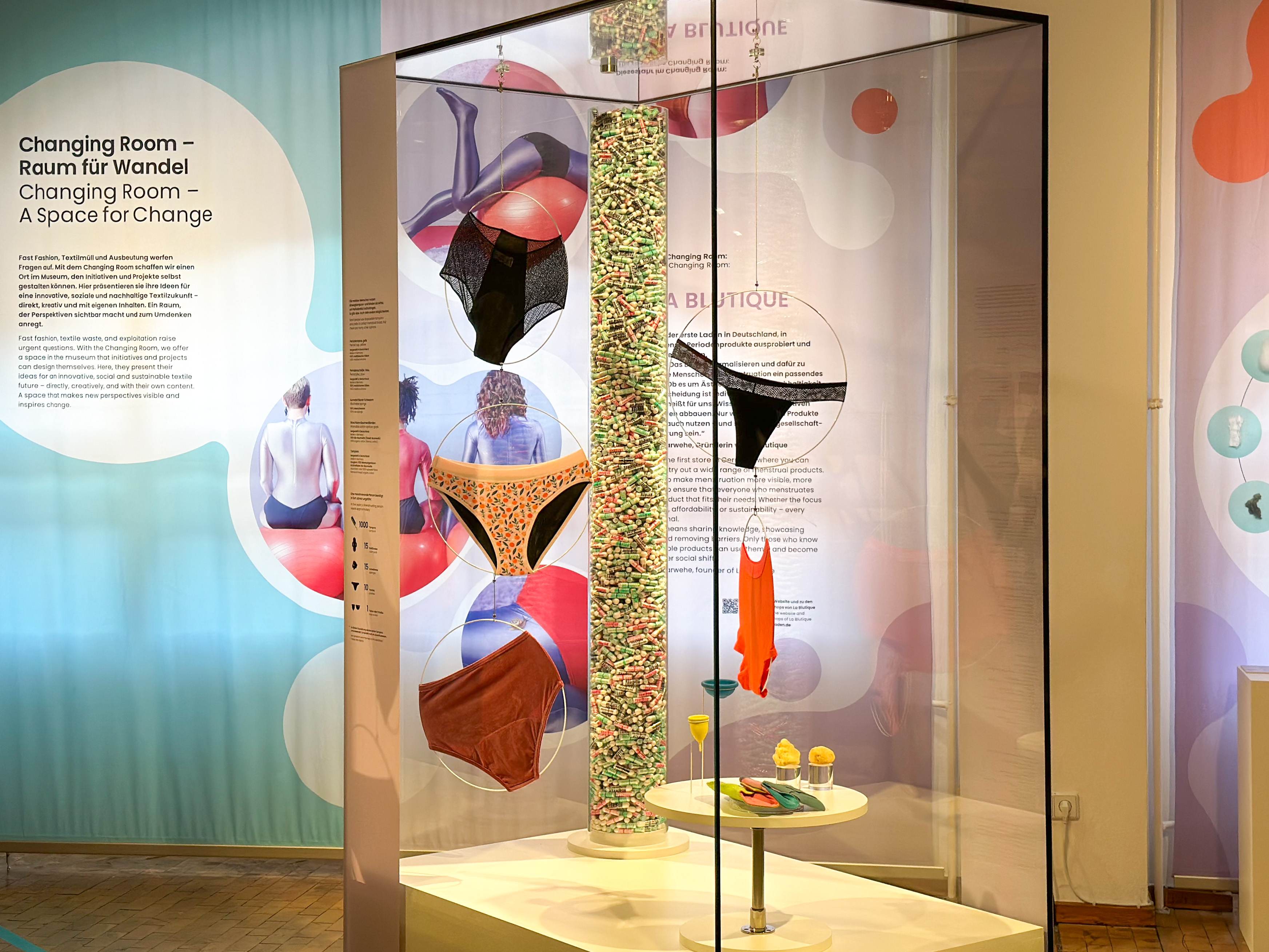 Blick auf die Vitrine im Ausstellungsbereich "Changing Room": Zu sehen sind verschiedene Modelle von Perioden-Unterwäsche, Textil-Binden, Menstruations-Cups und Tampons. Blick auf die Vitrine im Ausstellungsbereich "Changing Room": Zu sehen sind verschiedene Modelle von Perioden-Unterwäsche, Textil-Binden, Menstruations-Cups und Tampons. Im Hintergrund ist der Schriftzug "Changing Room" zu lesen.