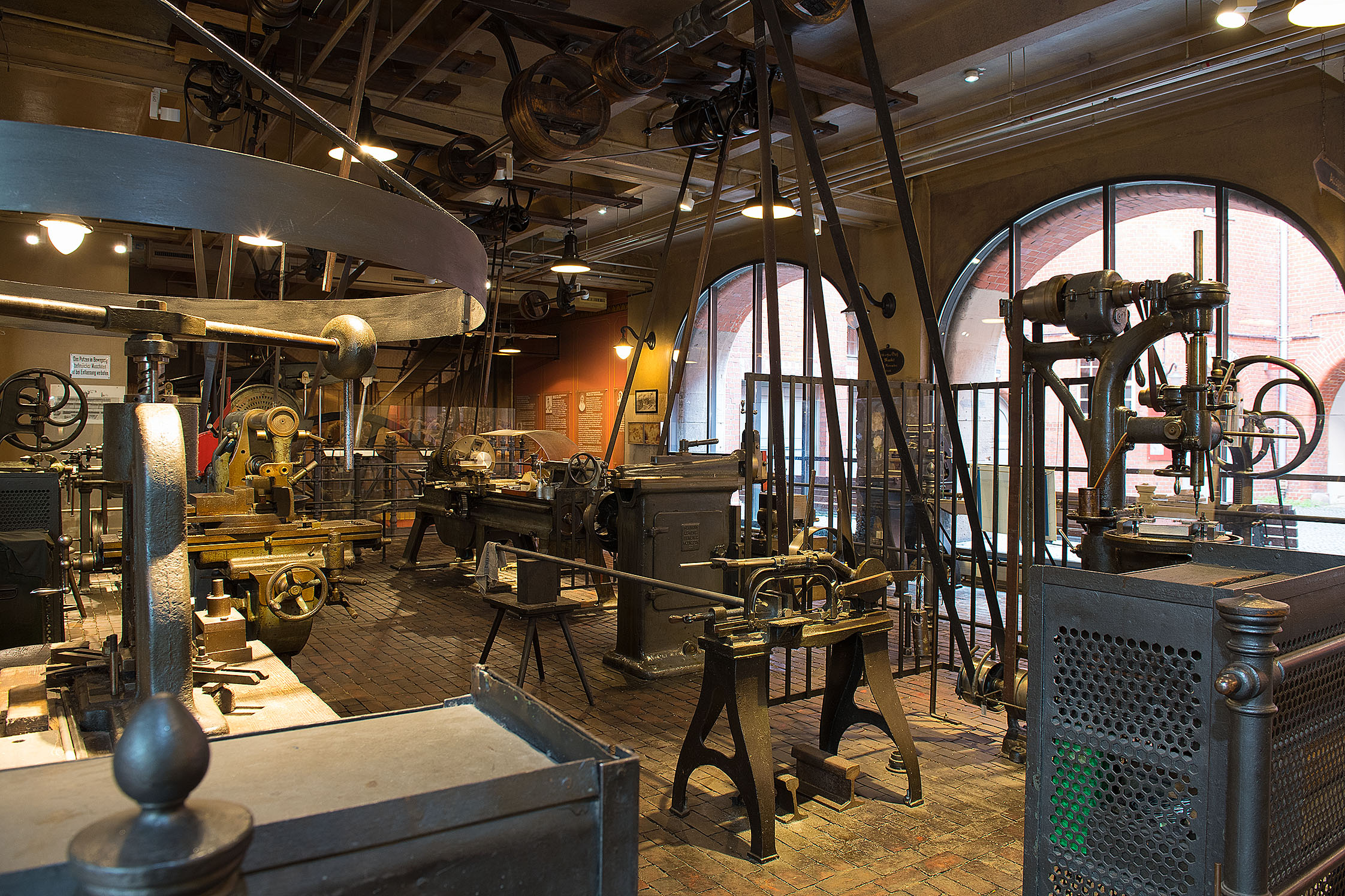 Ein Blick in die historische Werkstatt: Hier stehen verschiedene Maschine zur Metallbearbeitung. Oben an der Decke sind die verschiedenen Räder und der Transmissionsriemen zu sehen, die die Maschinen durch eine Dampfmaschine antreiben.