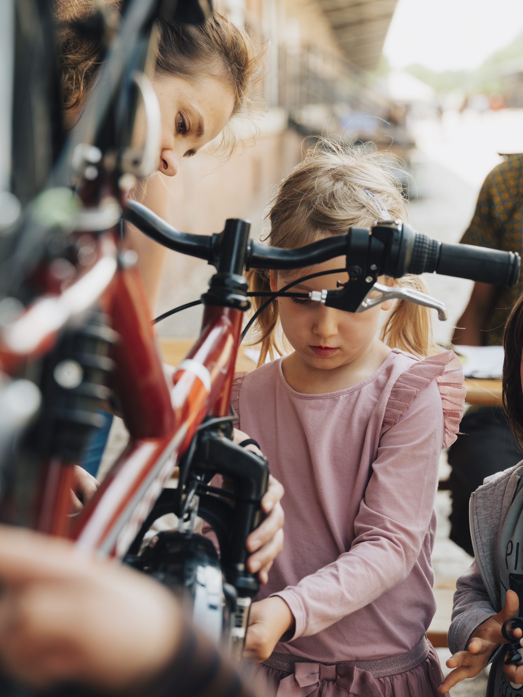 Ein Mädchen steht an einem montierten Fahrrad und repariert es mit Hilfe einer erwachsenen Frau