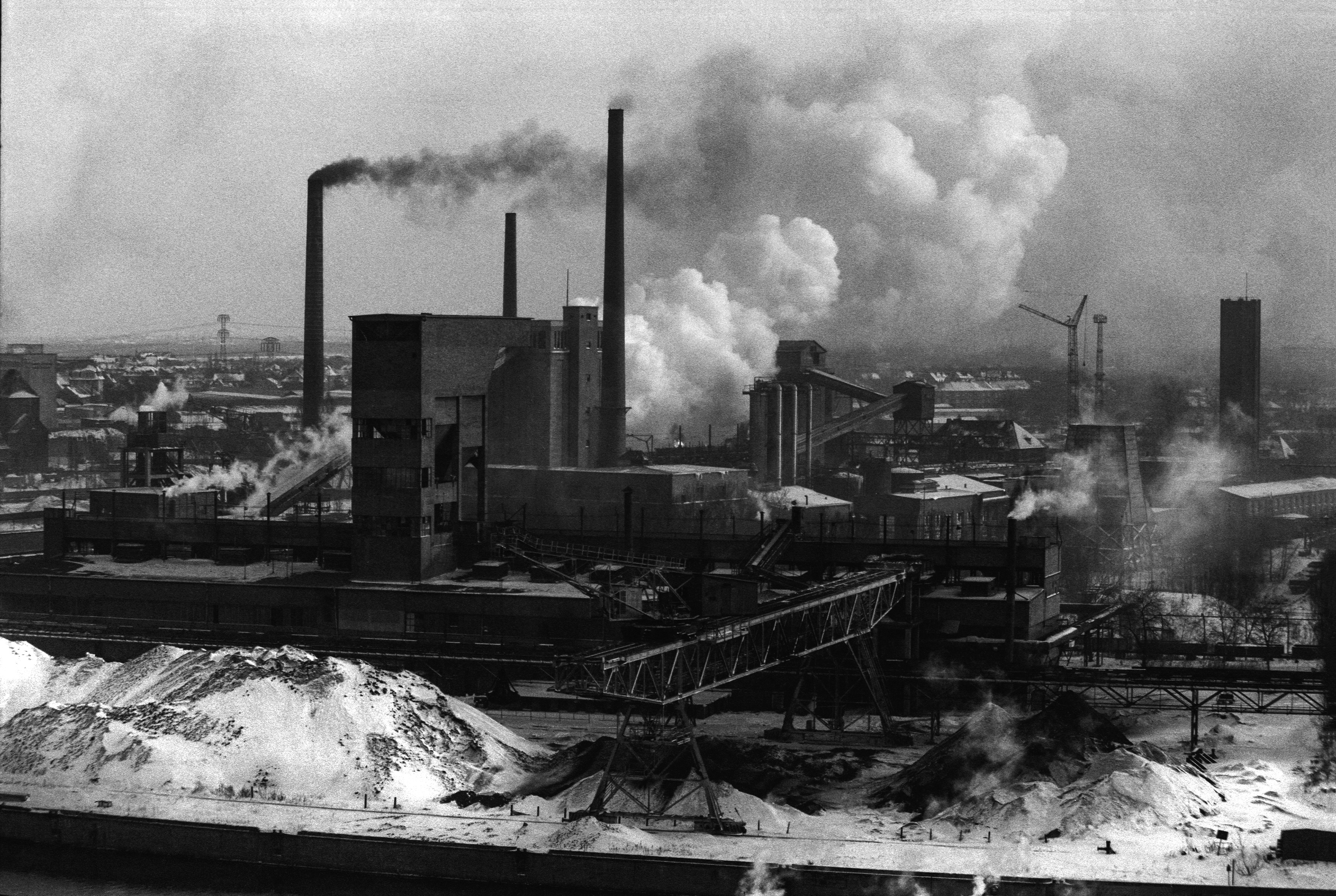 Auf dem Foto ist ein Kraftwerk zu sehen, aus dessen Schornsteinen dichter Rauch aufsteigt.