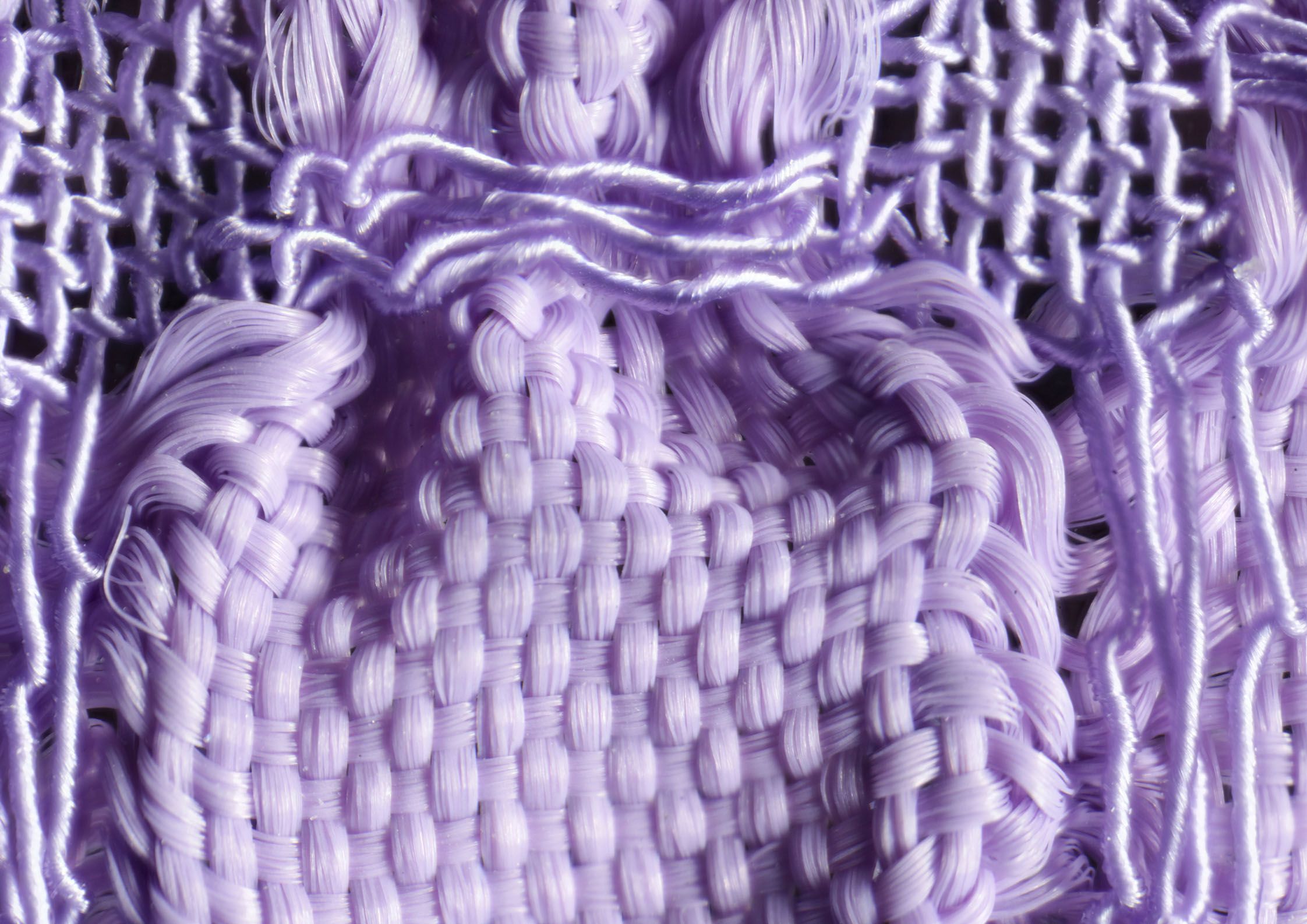 Detailaufnahme eines lilafarbenen Gewebes. Durch zwei unterschiedlich elastische Garne, Gummilitze und Seide, tritt das Blasenmuster des Stoffes besonders hervor. 