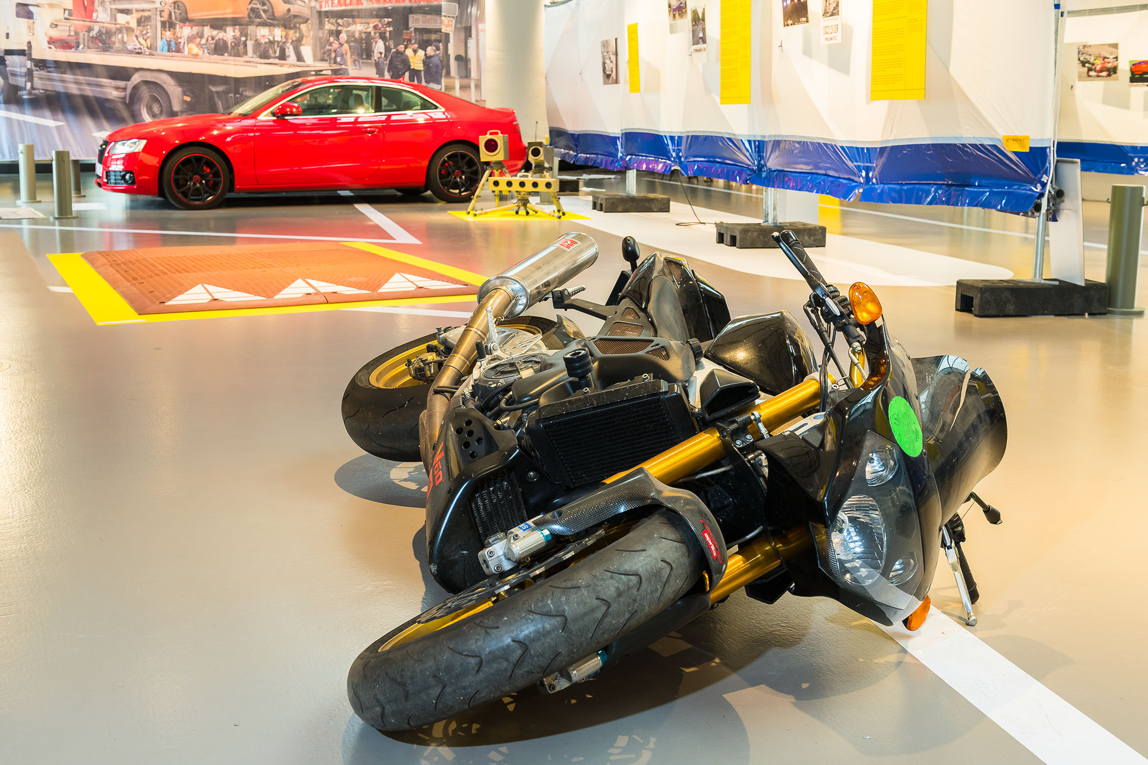 Ein schwarzes Motorrad liegt auf dem Boden, im Hintergrund ist ein rotes Auto zu sehen.