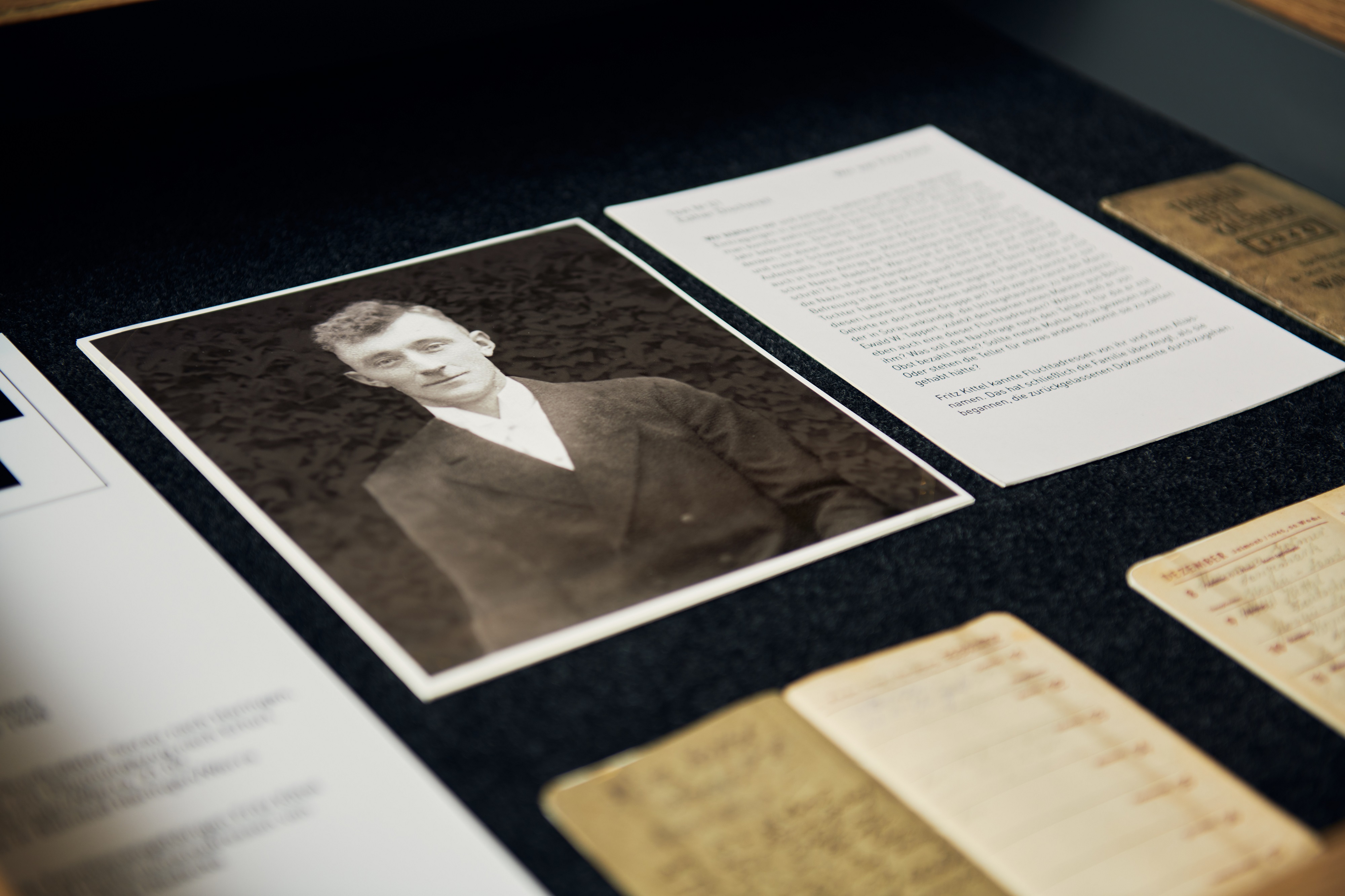 Eine geöffnete Schublade. Zu sehen ist eine schwarzweiße Fotografie eines jungen Mannes im weißen Hemd und dunklen Jackett. Daneben ist ein maschinenbeschriebenes Stück Papier zu erkennen. Der Name "Fritz Kittel" ist lesbar.