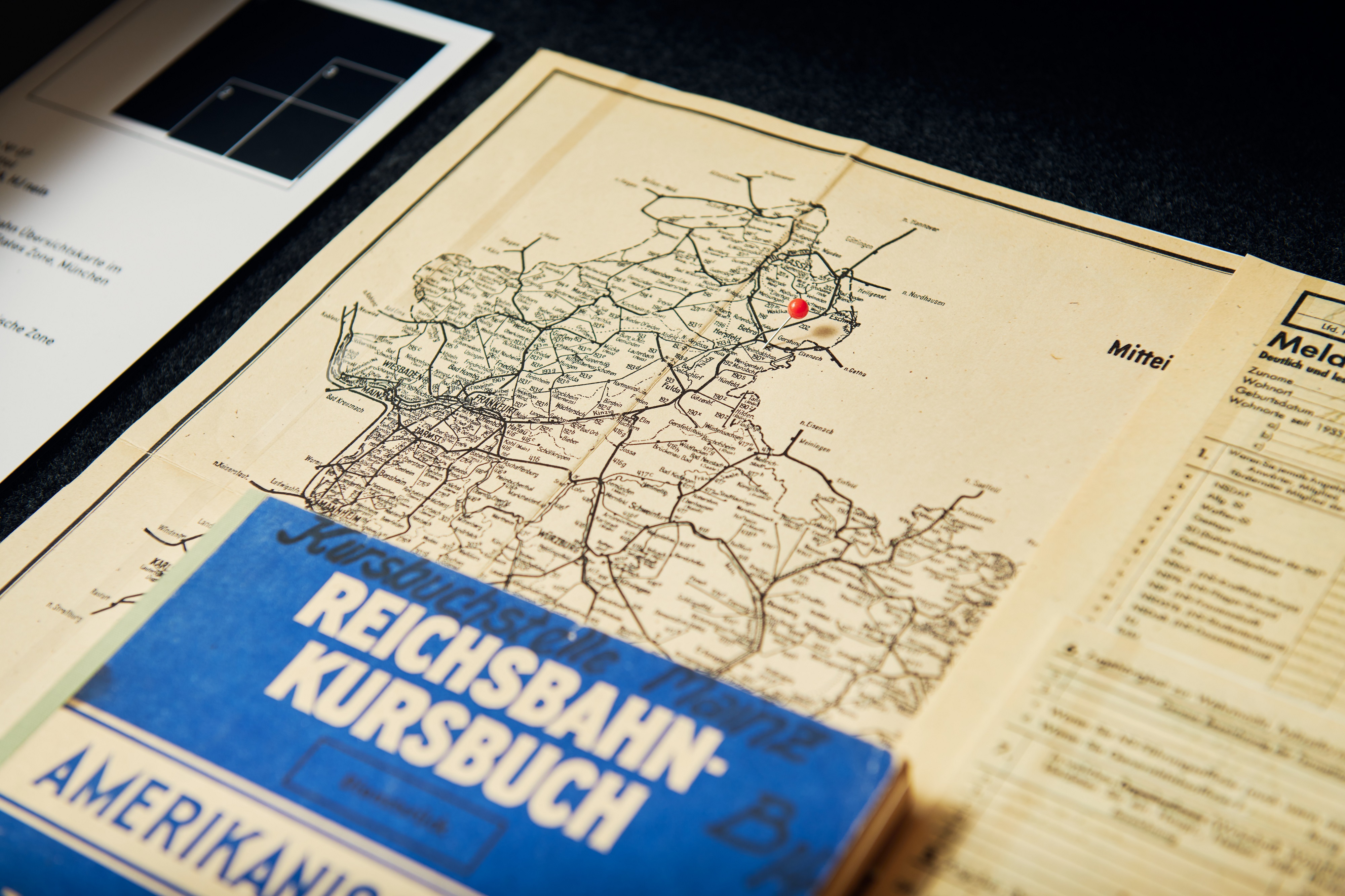 Eine Landkarte mit Bahn-Streckennetzen, zu erkennen sind die Städte Frankfurt und Wiesbaden. Darüber liegt ein blaues Buch mit der Aufschrift "Reichsbahn Kursbuch".