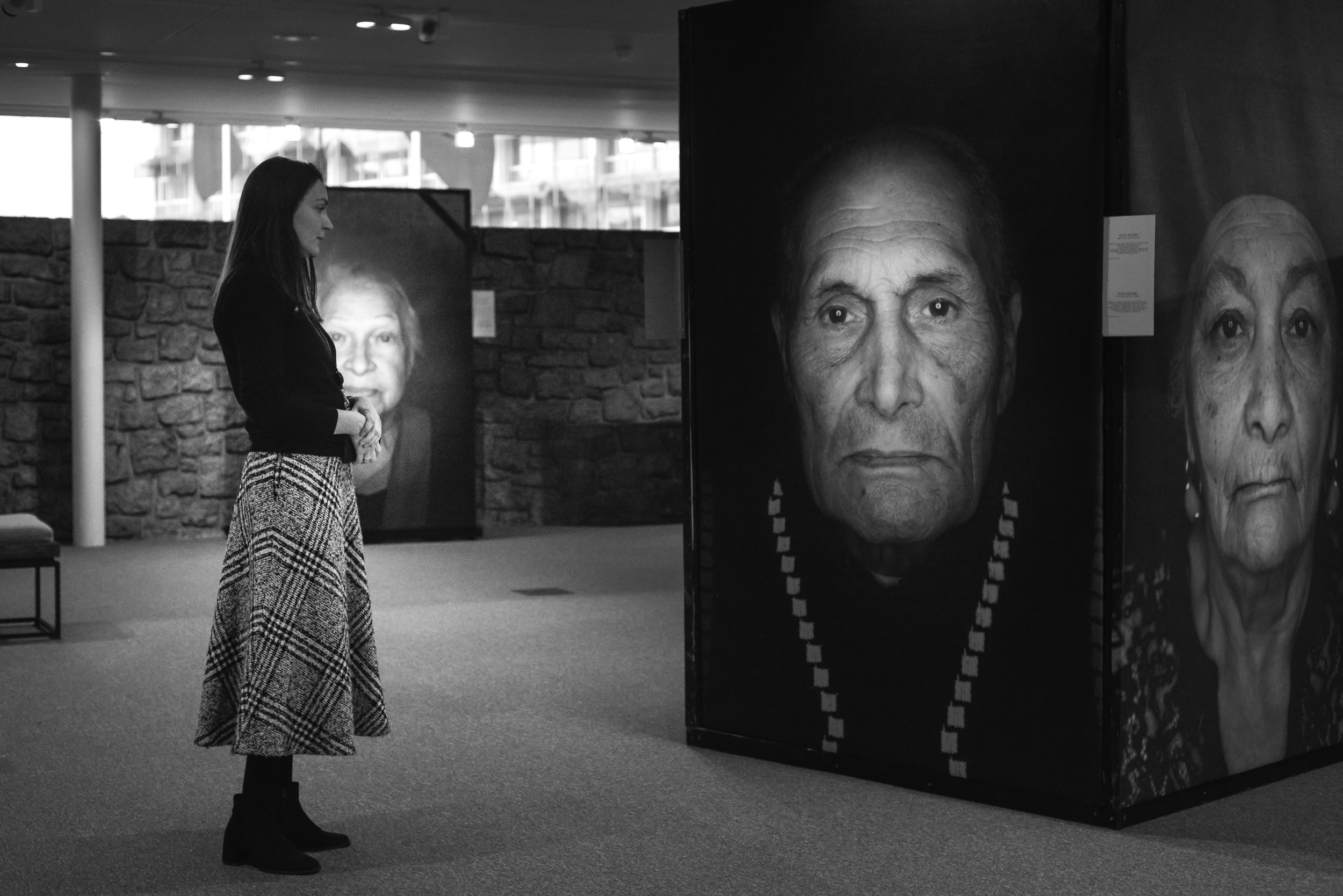 Blick in die Ausstellung "Ma Bistrass". Ein Schwarz-Weiß-Foto. Eine Person, die einen Rock trägt, steht vor einem großen Porträt-Foto einer Überlebenden der nationalsozialistischen Verfolgung.