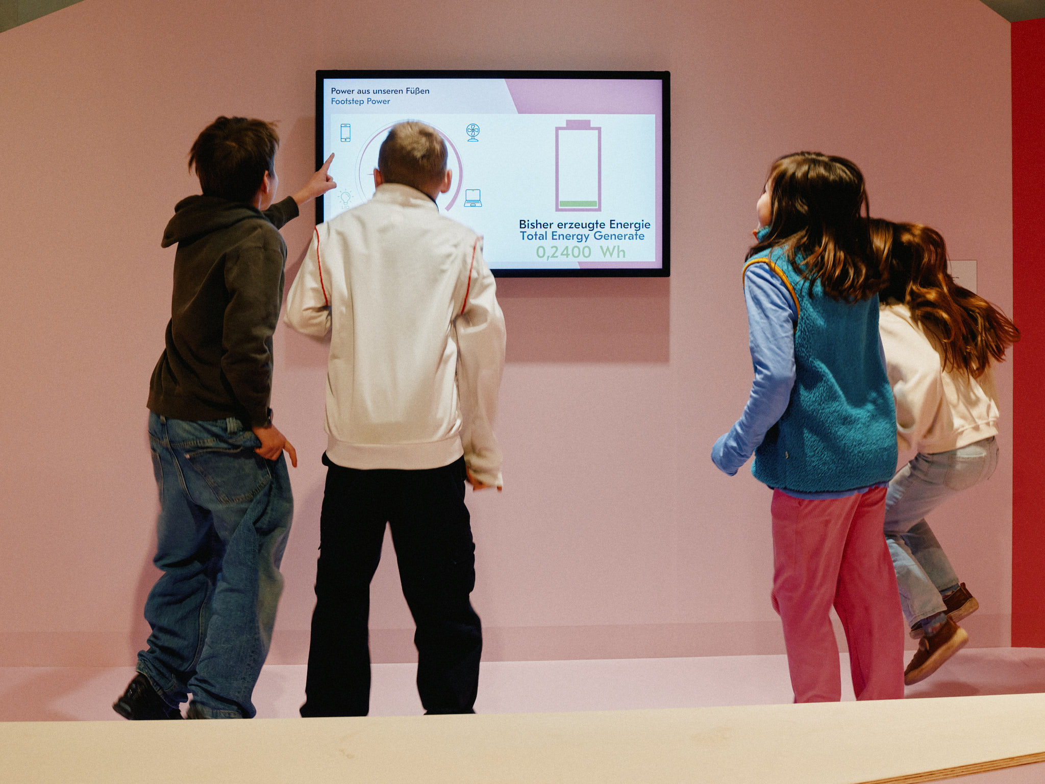 Zwei Mädchen und zwei Jungen hüpfen fröhlich in die Luft. Vor ihnen ein Display, das anzeigt, wie viel Energie sie dabei erzeugen.
