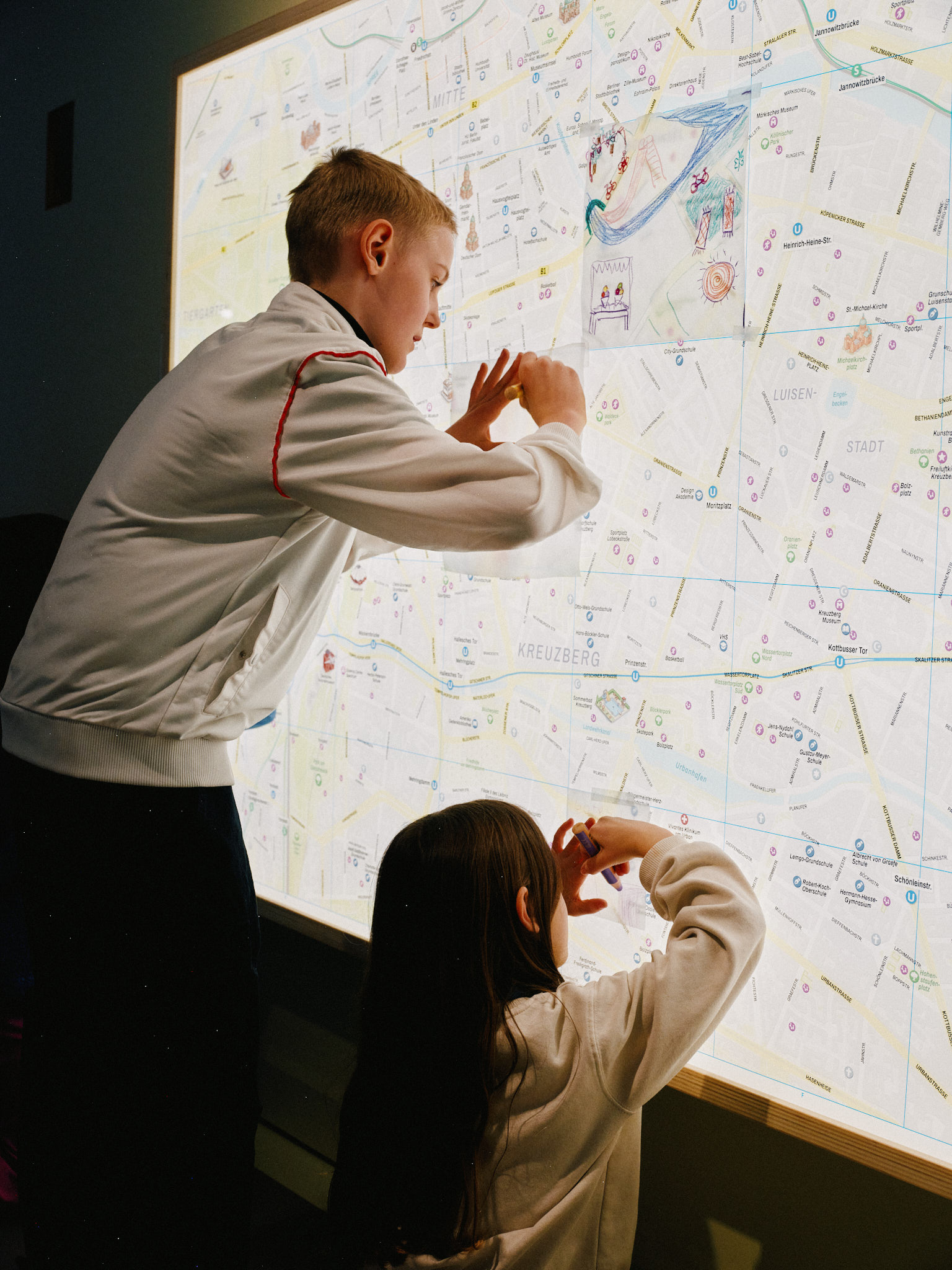 Auf einem hinterleuchteten Stadtplan können Kinder alternative Stadtpläne bemalen und darüber kleben. Ein Mädchen und ein Junge sind fleißig dabei.